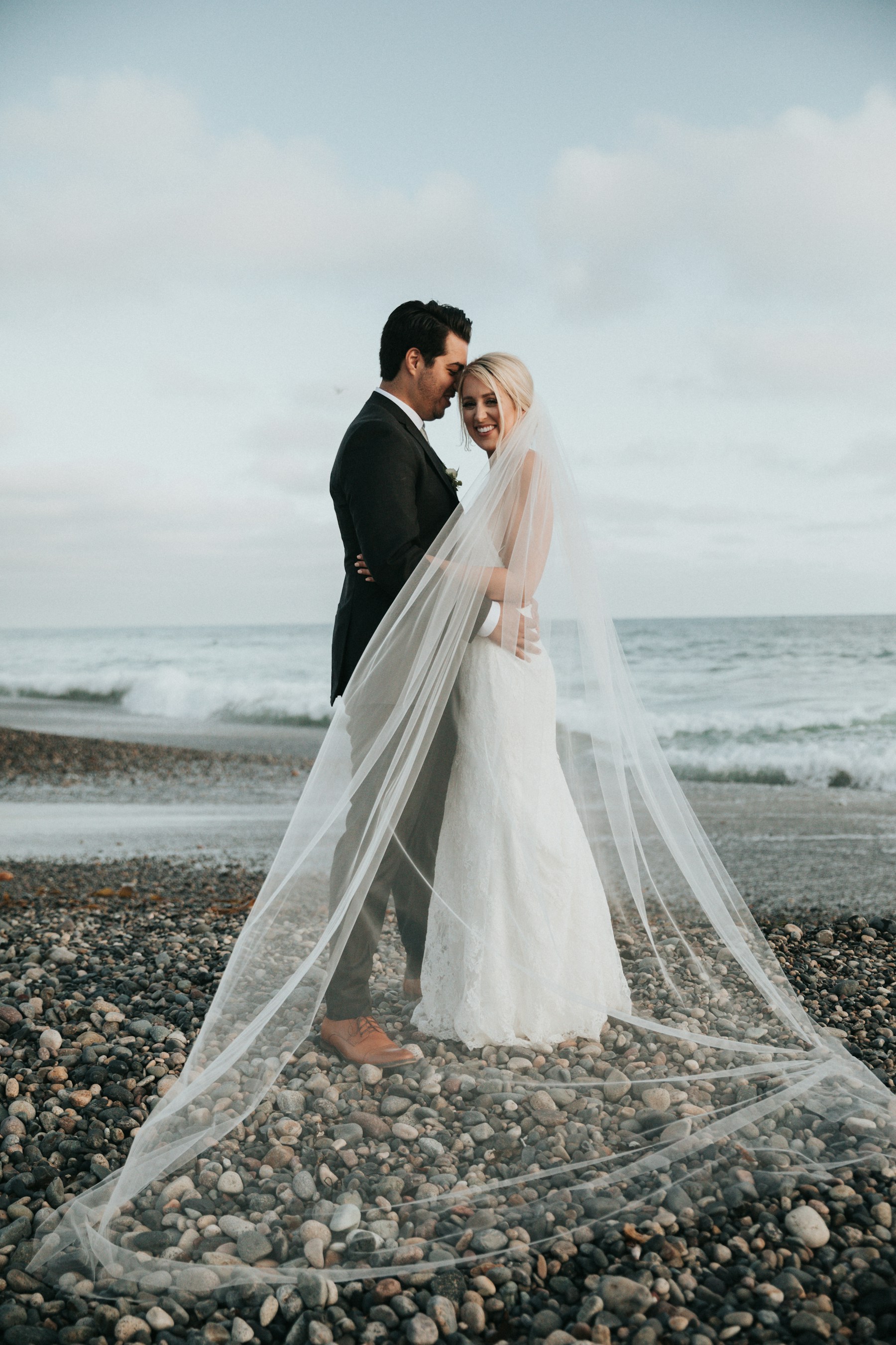 Casal de noivos abraçado à beira do mar